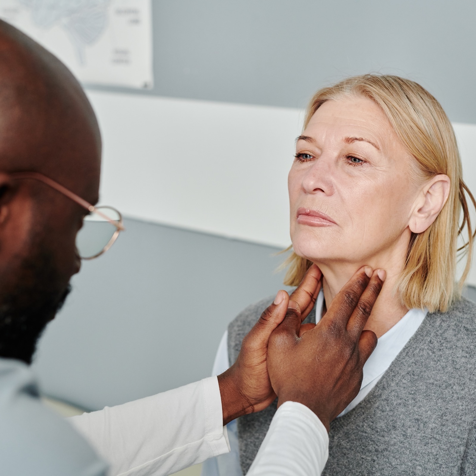 Medico examinando con las manos el cuello de una paciente durante una consulta de tiroides