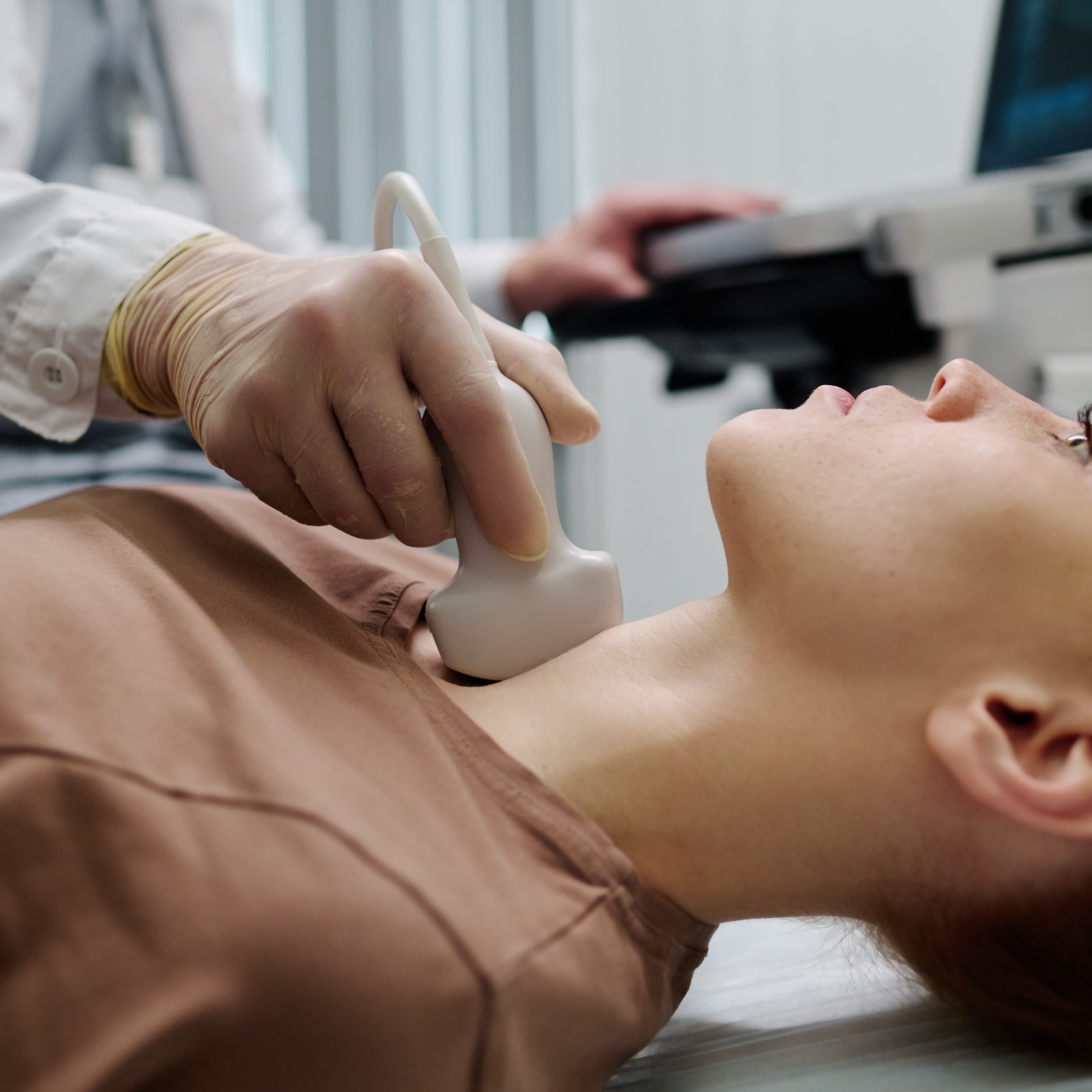 Medico realizando un ultrasonido de tiroides con el transductor sobre el cuello de la paciente