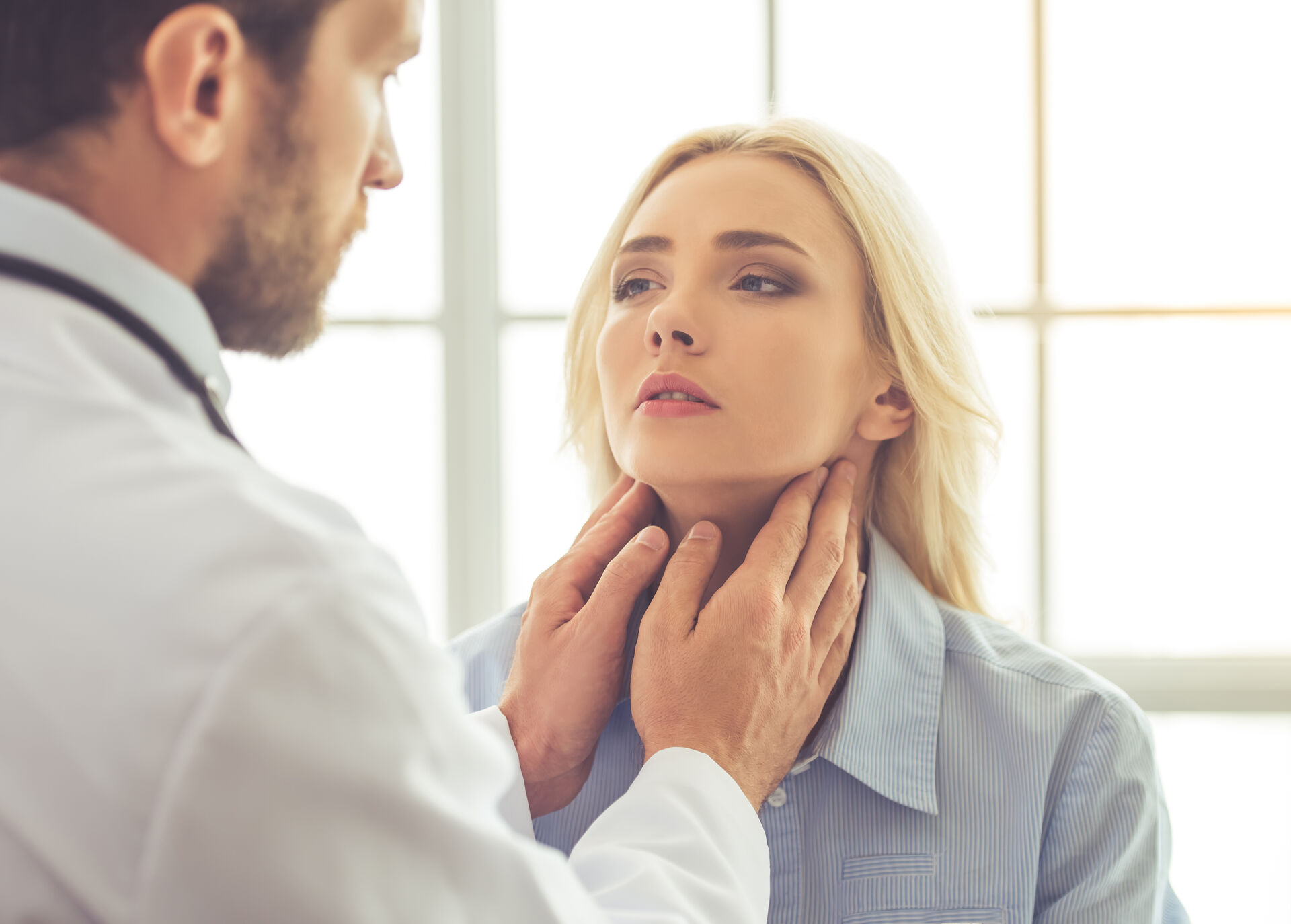 Médico revisando la tiroides de una paciente en consulta